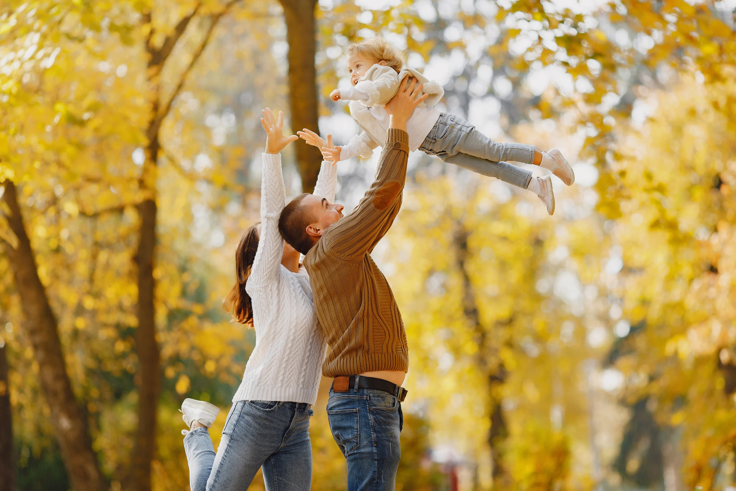 Family playing in an autumn park, parents lifting their child into the air